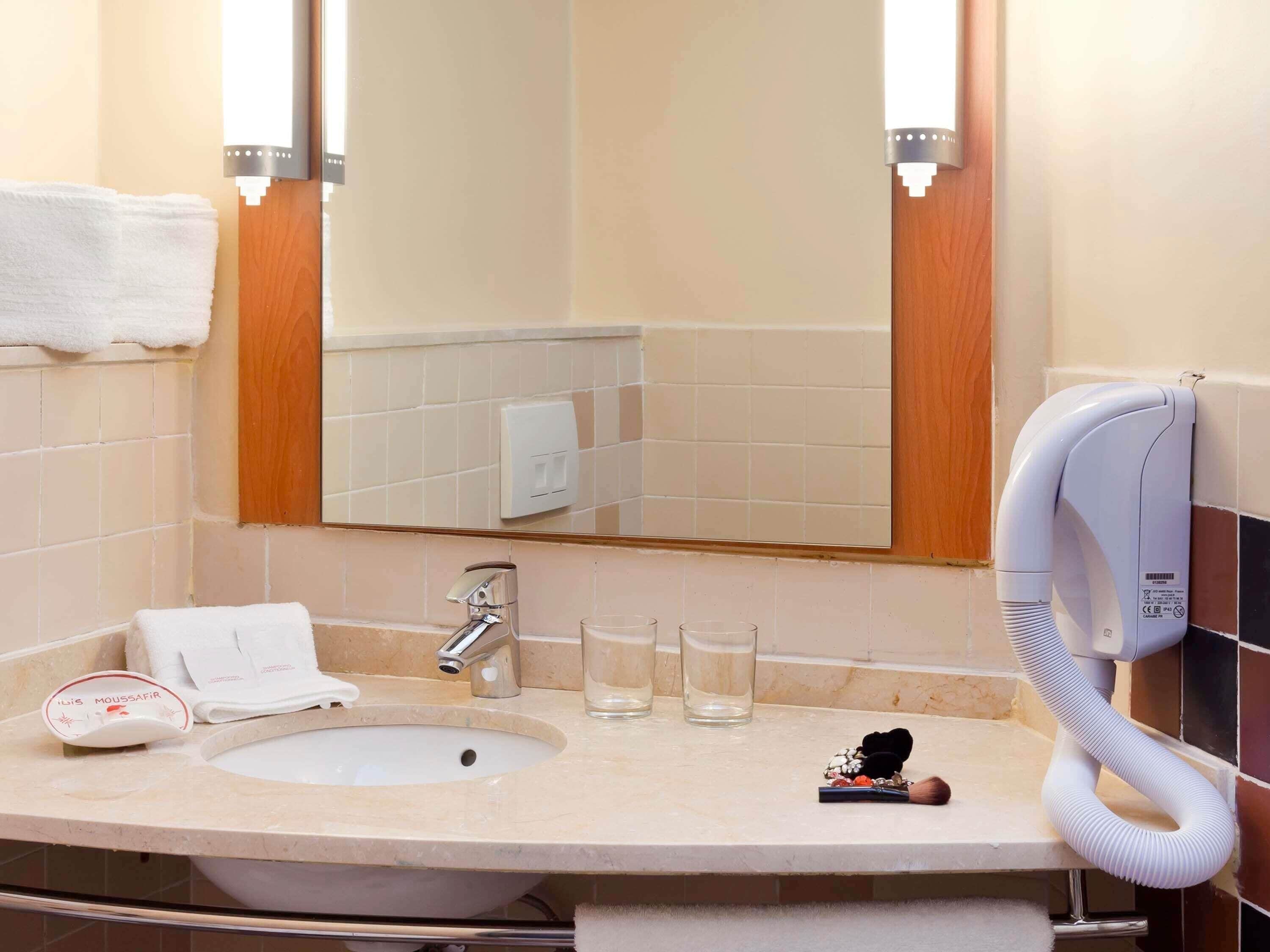Une salle de bain équipée d’un lavabo, d’un miroir, d’un porte-serviettes et d’un sèche-cheveux.