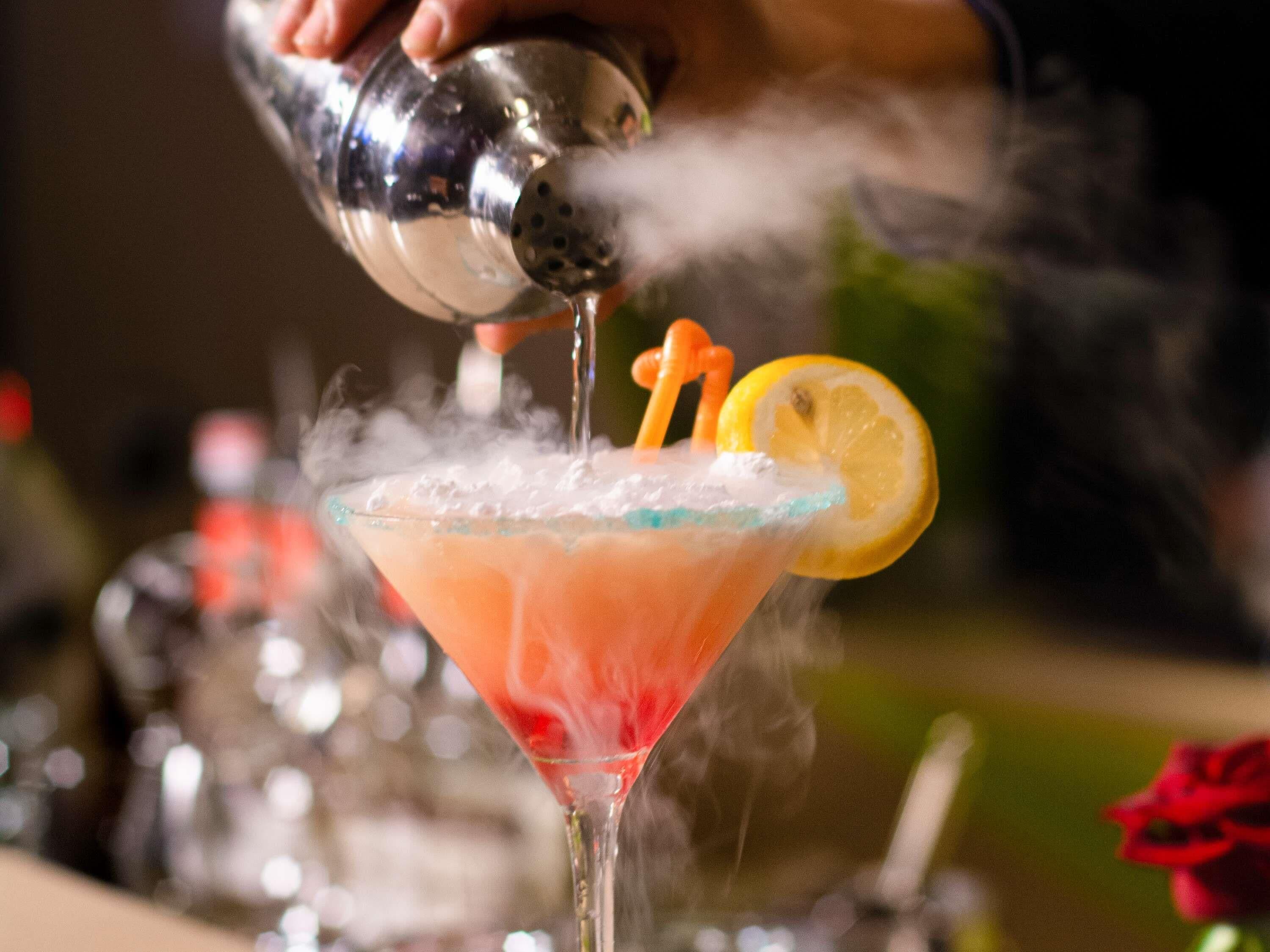 A cocktail being poured into a glass with a lemon slice garnish.