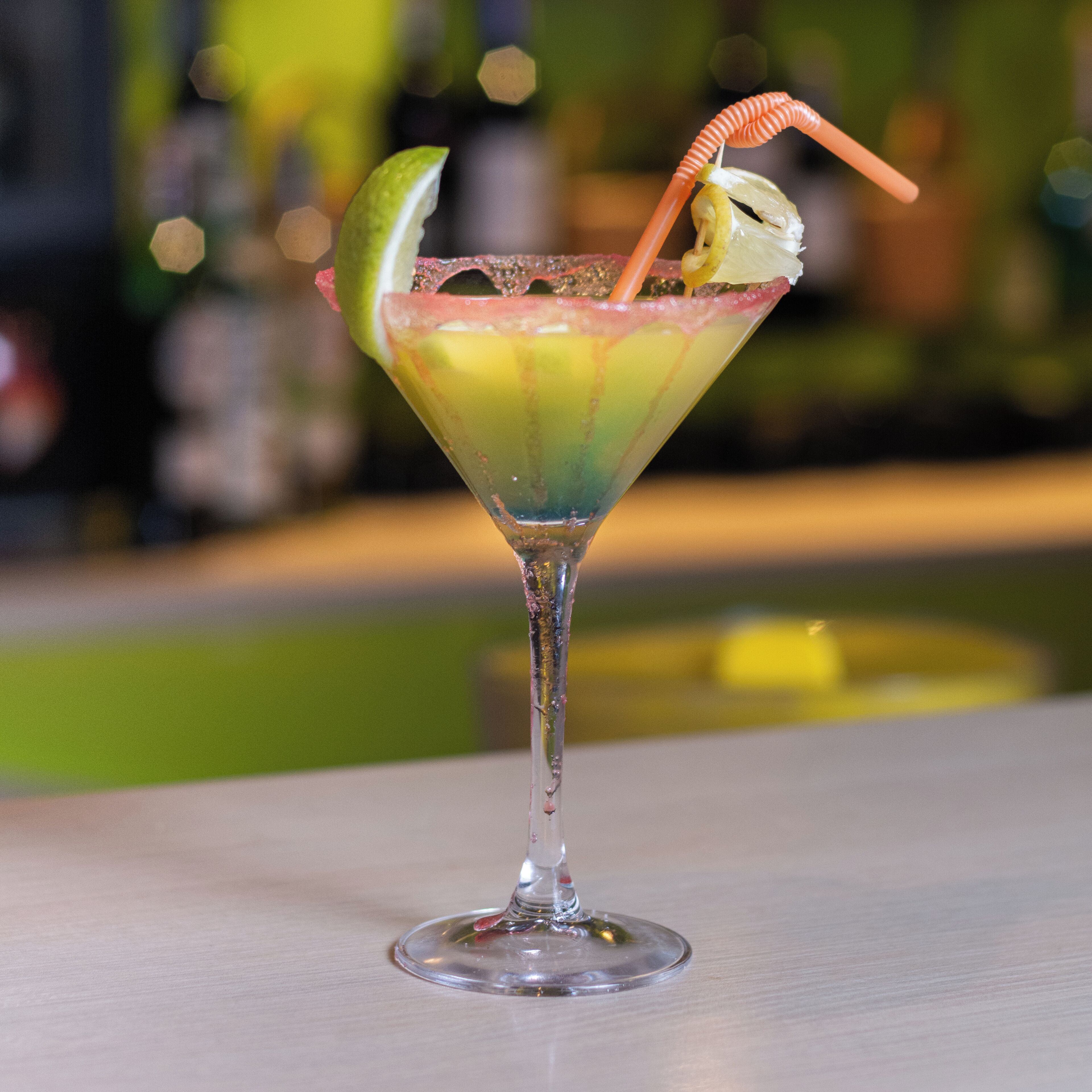 Un cóctel en una copa de martini con una rodaja de lima y una pajita.