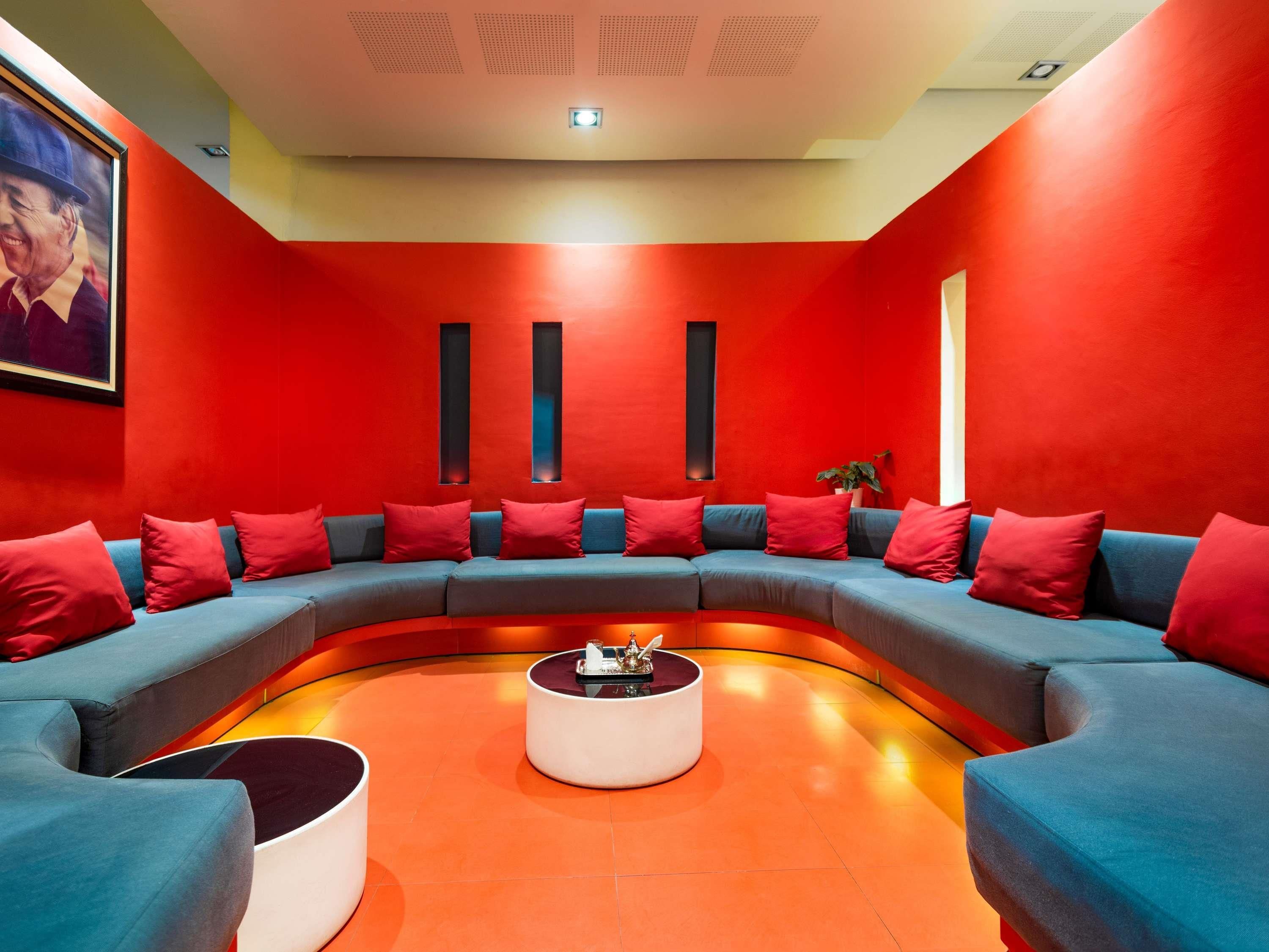 A modern lounge area with a curved blue sofa set, red cushions, and a central white coffee table.