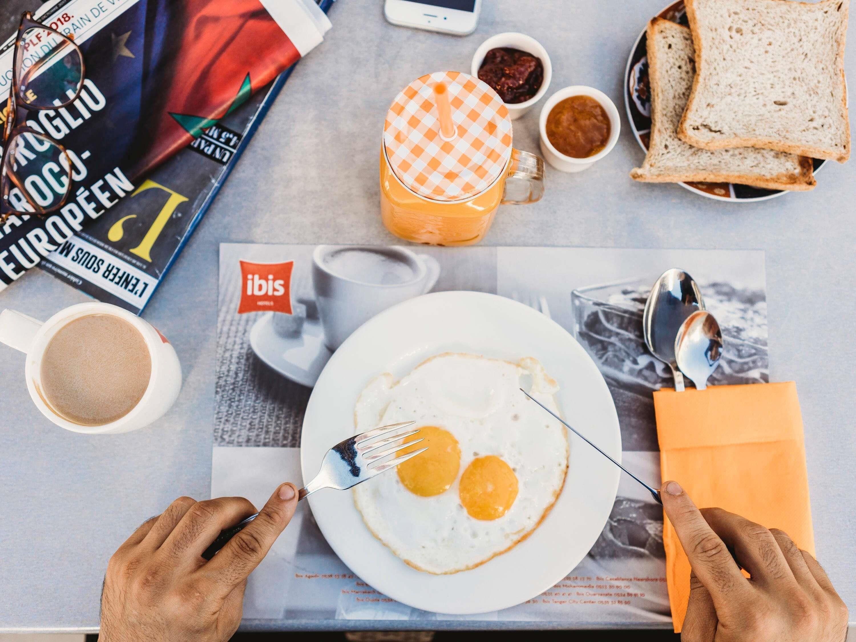 A breakfast setting with a plate of eggs, toast, and coffee, along with a magazine and a smartphone on the table.