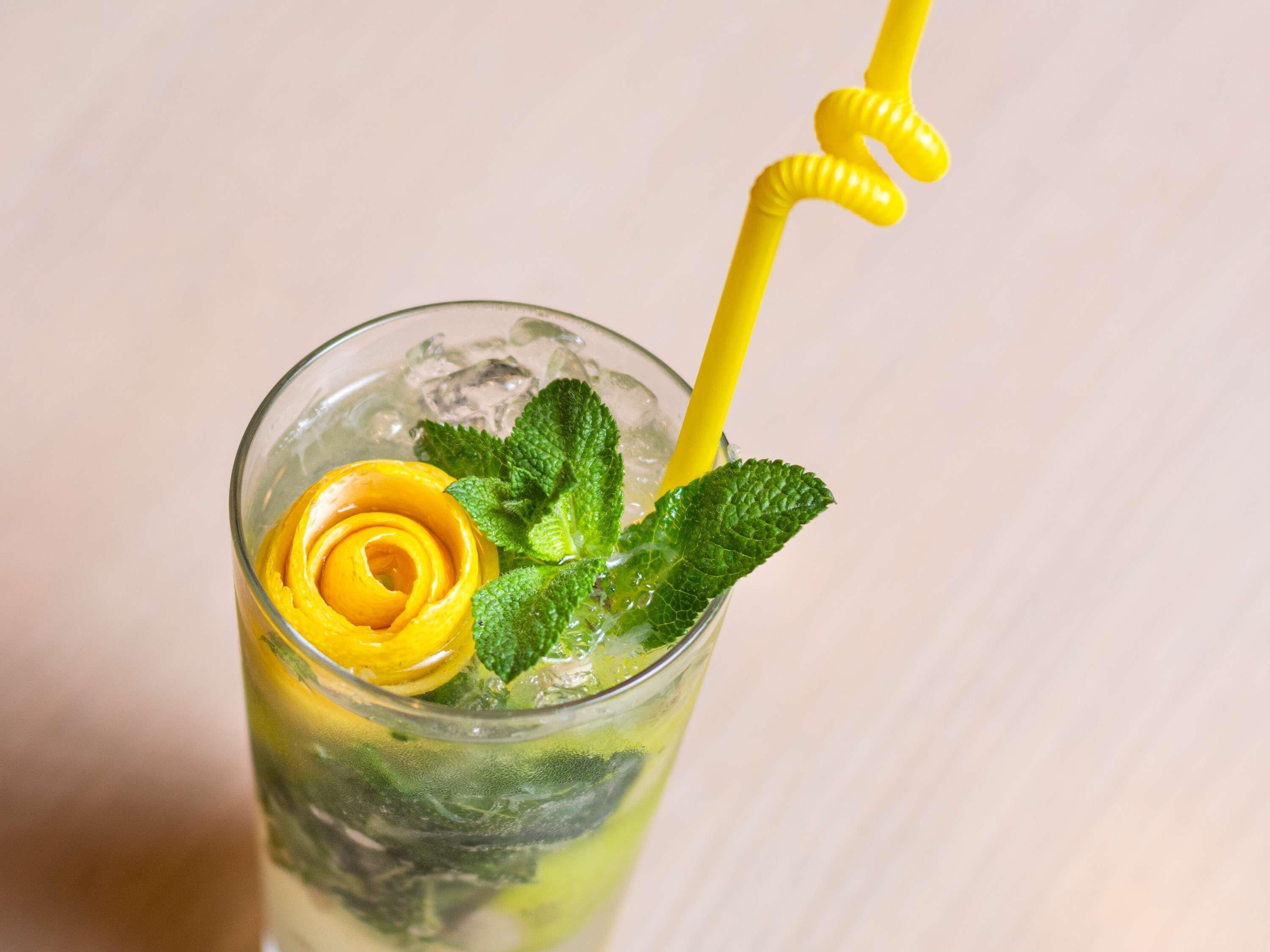 A glass with a yellow straw, mint leaves, and a lemon slice.