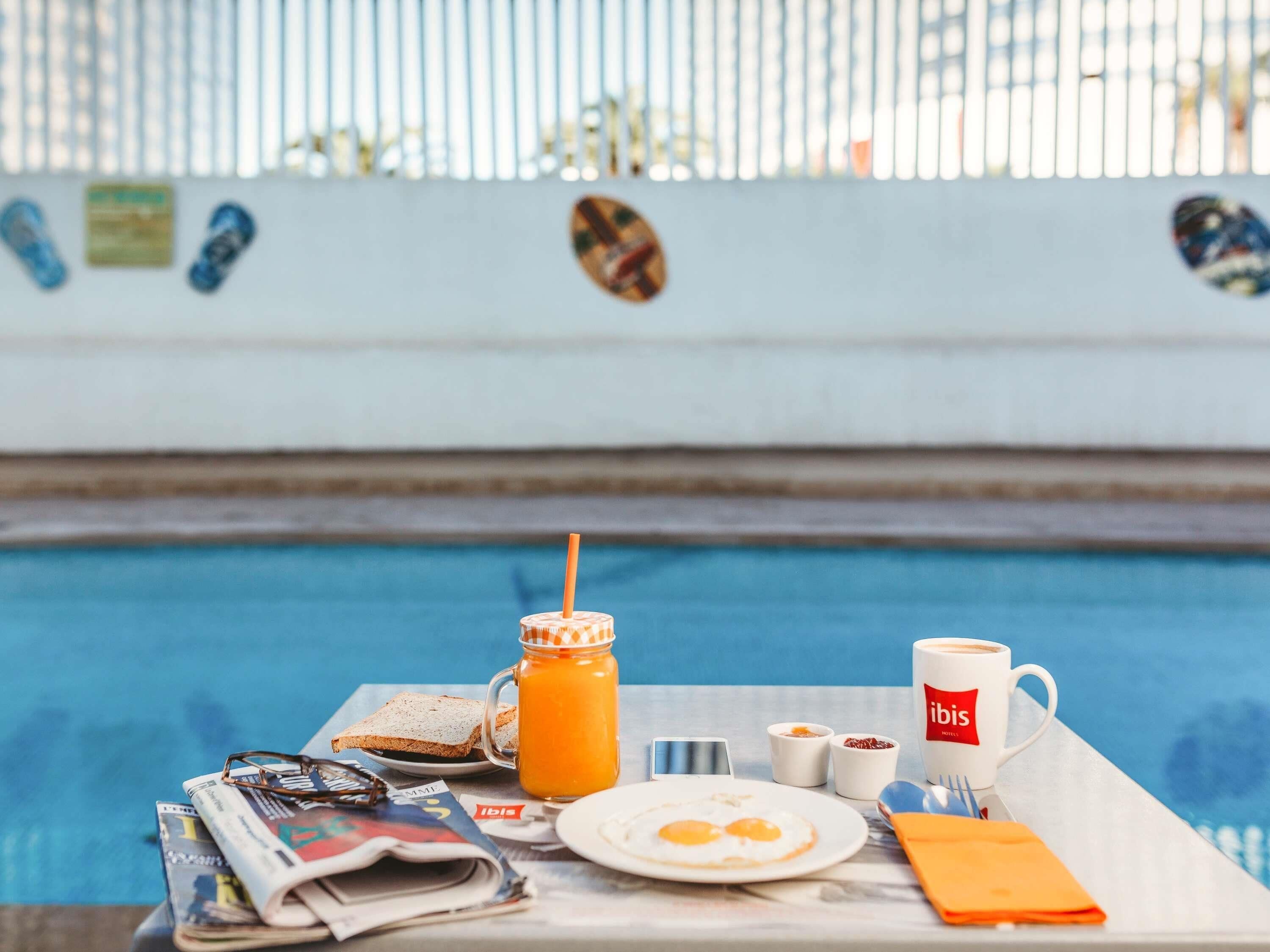 Een ontbijt bij het zwembad, compleet met krant, toast, eieren, sap en een koffiemok.