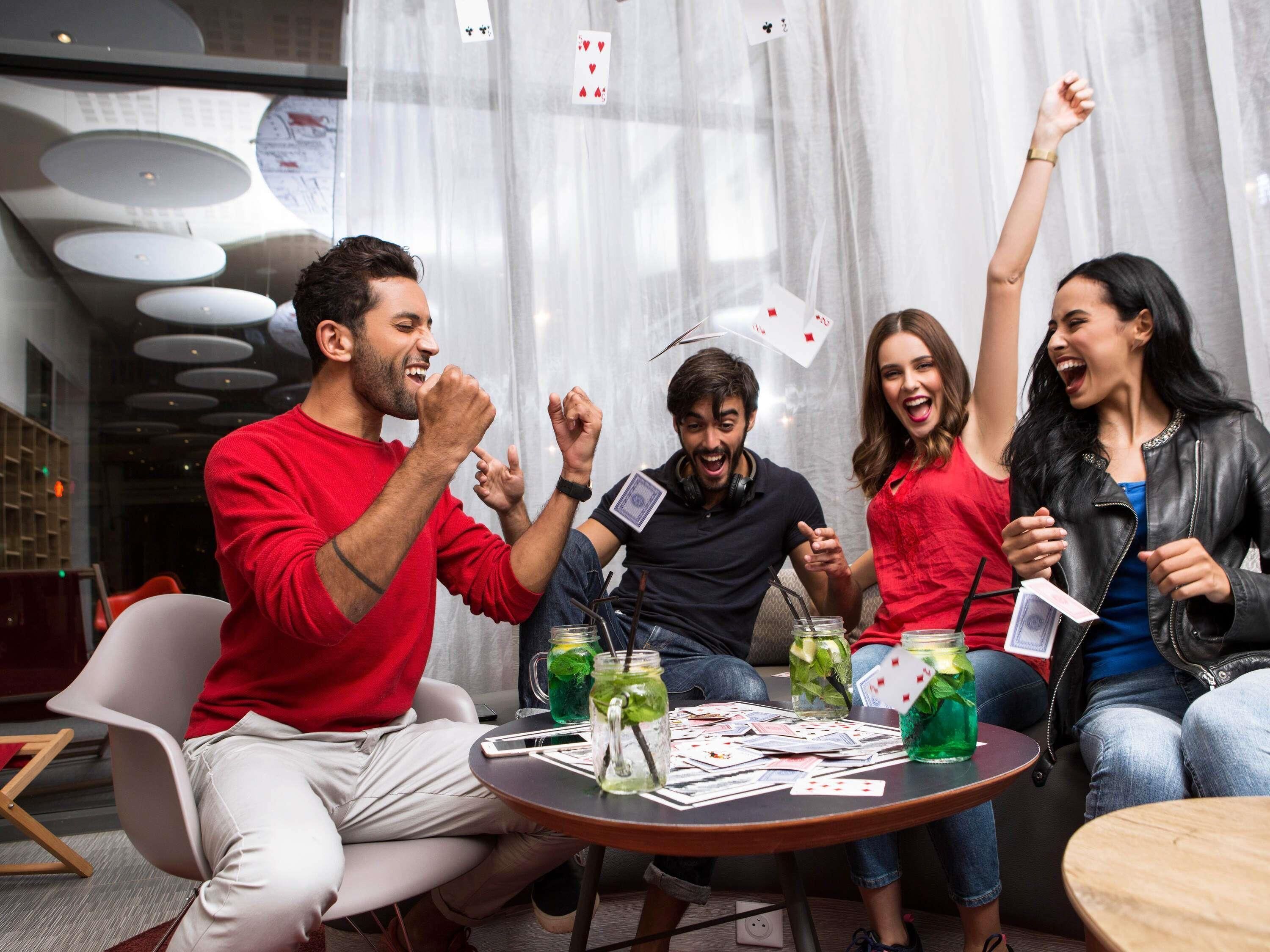 A group of people playing cards at a table with drinks and cards scattered on it.