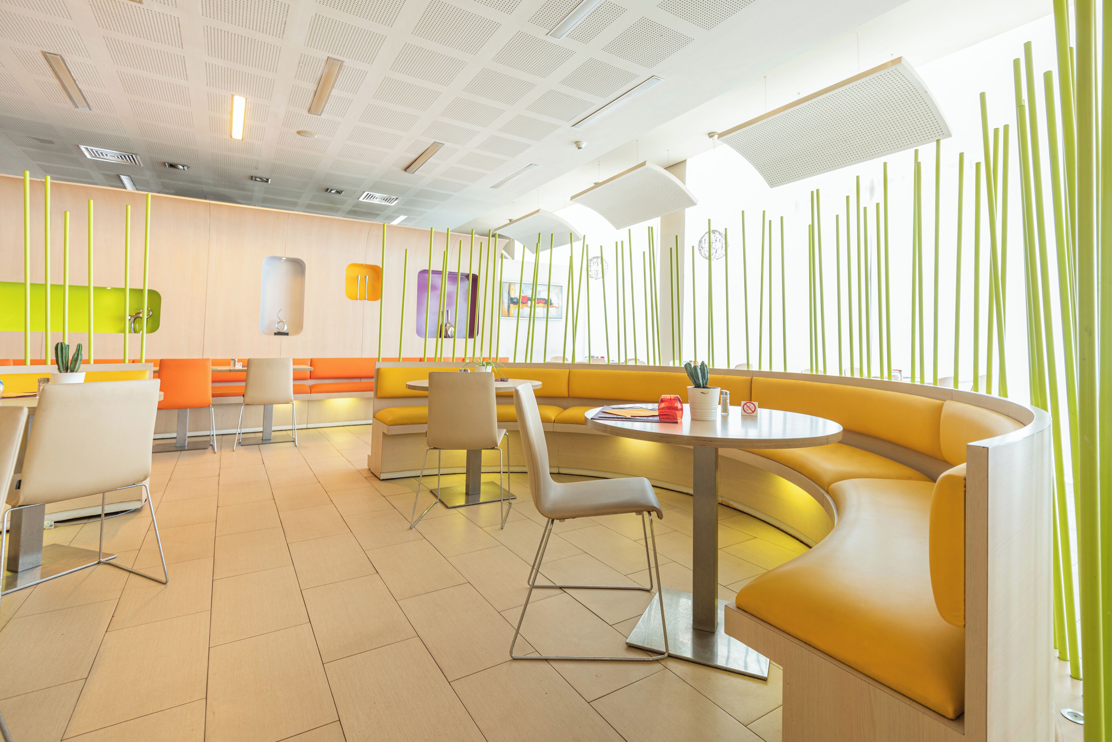 A modern restaurant with yellow and orange seating, a curved table, and a ceiling with recessed lighting.