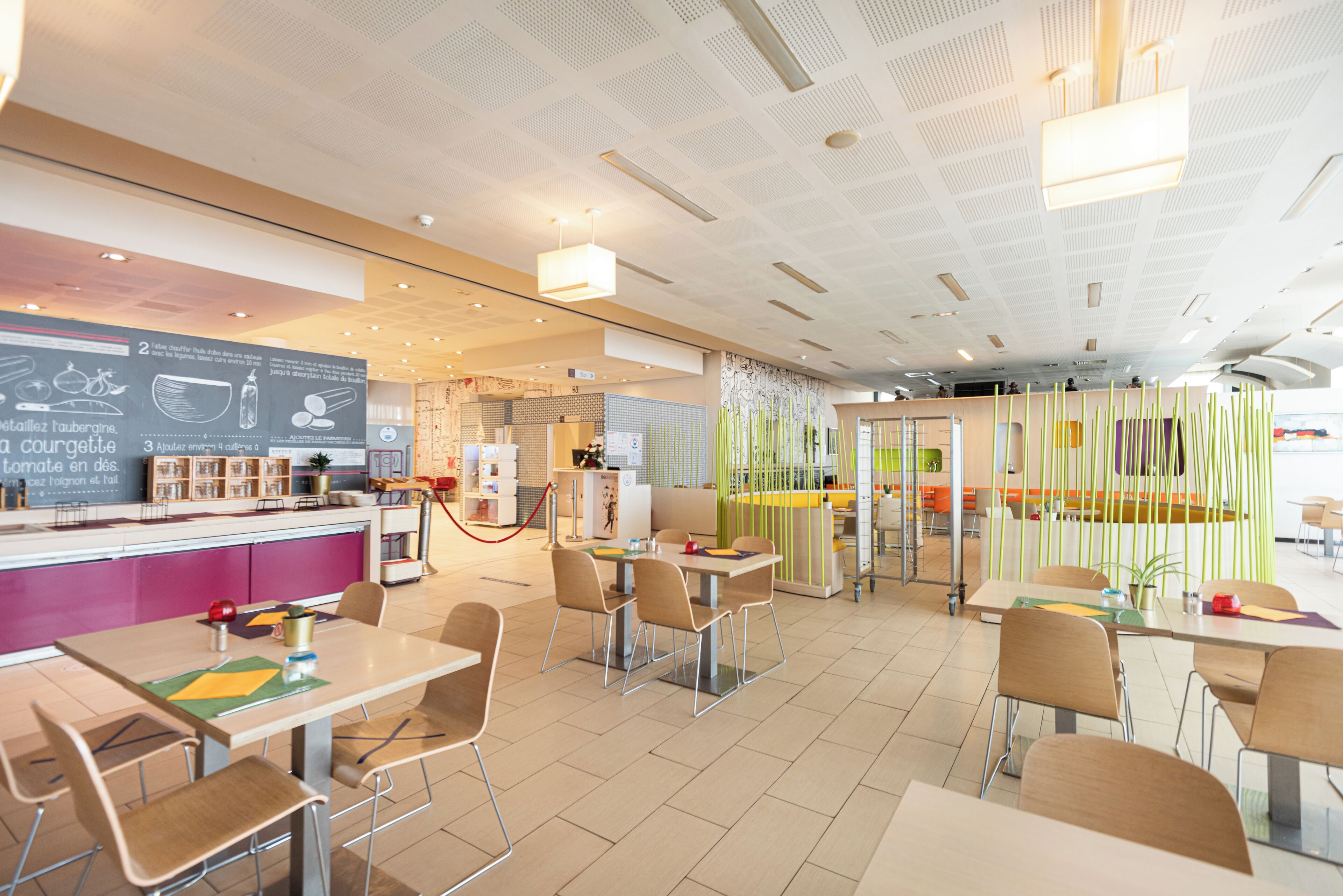 A modern restaurant with a counter, tables, chairs, and a ceiling with recessed lighting.