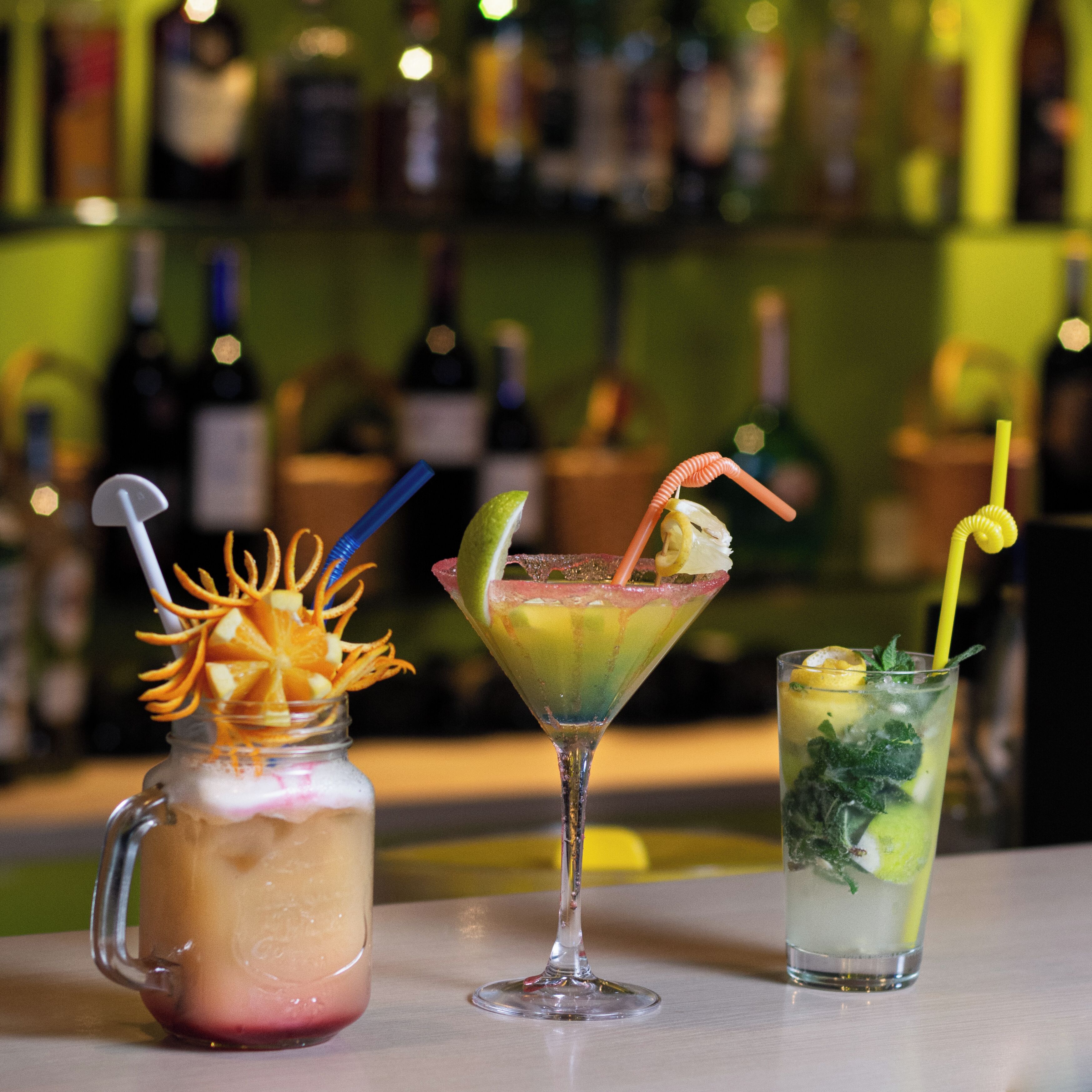 Tres bebidas sobre una barra, con un fondo borroso de botellas.
