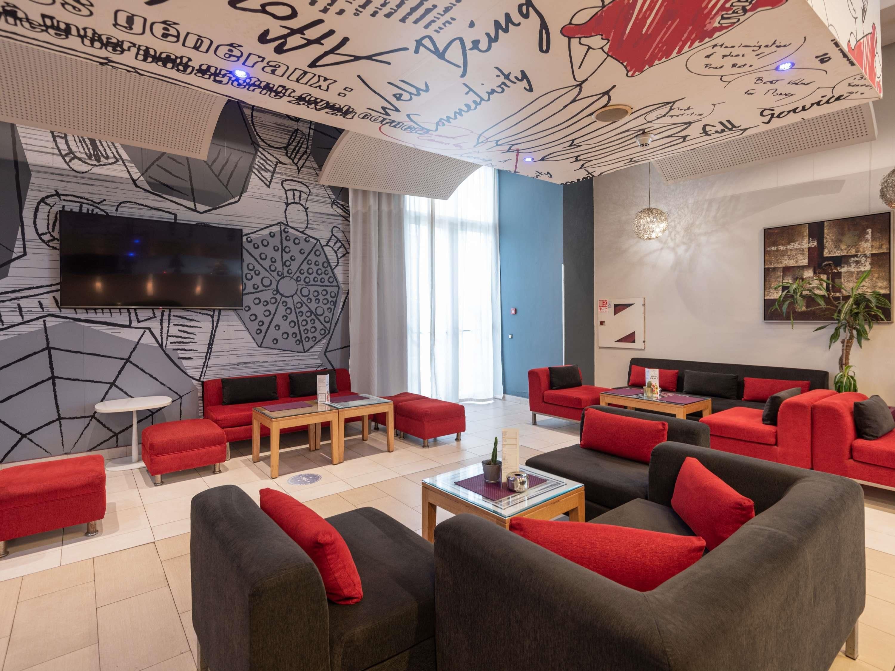 Un espacio de descanso moderno con sofás rojos y grises, un televisor de pantalla plana y un techo decorado con grafitis artísticos.