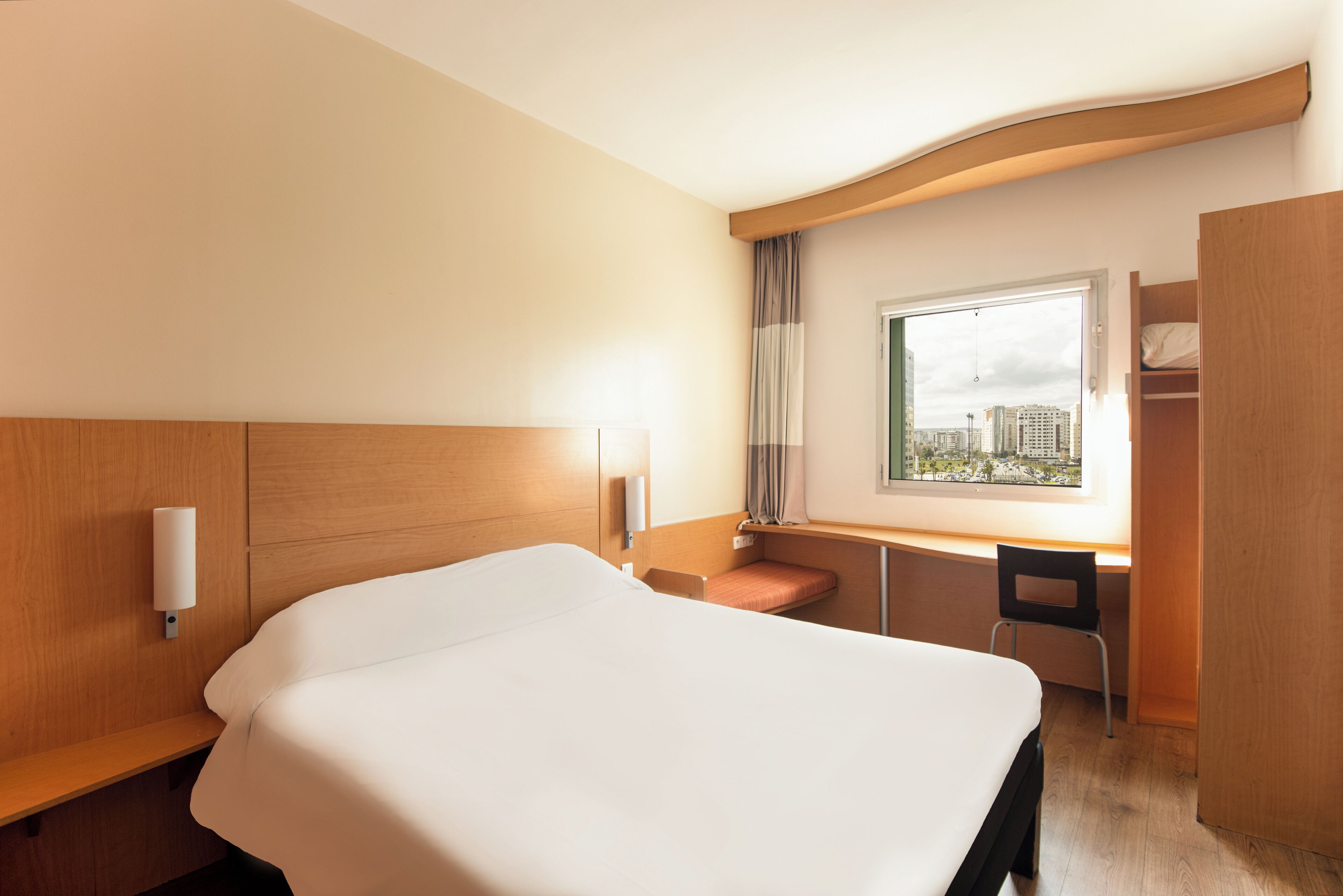 Een hotelkamer met een groot bed, een bureau, een stoel en een raam met uitzicht op de stad.