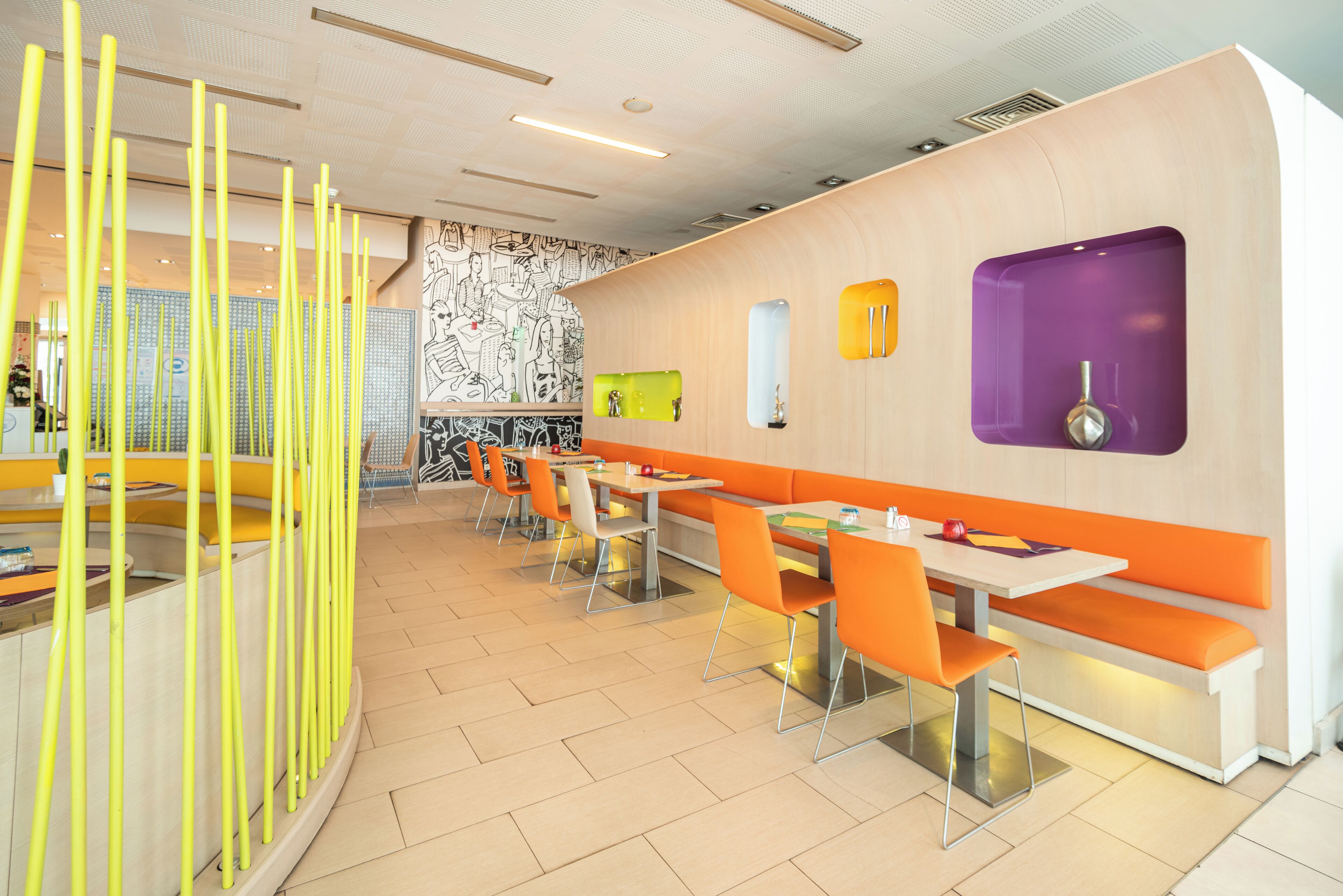Un restaurante moderno con cabinas y mesas color naranja, un papel tapiz y un adorno amarillo.