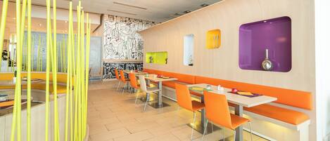 Un restaurante moderno con cabinas y mesas color naranja, un papel tapiz y un adorno amarillo.
