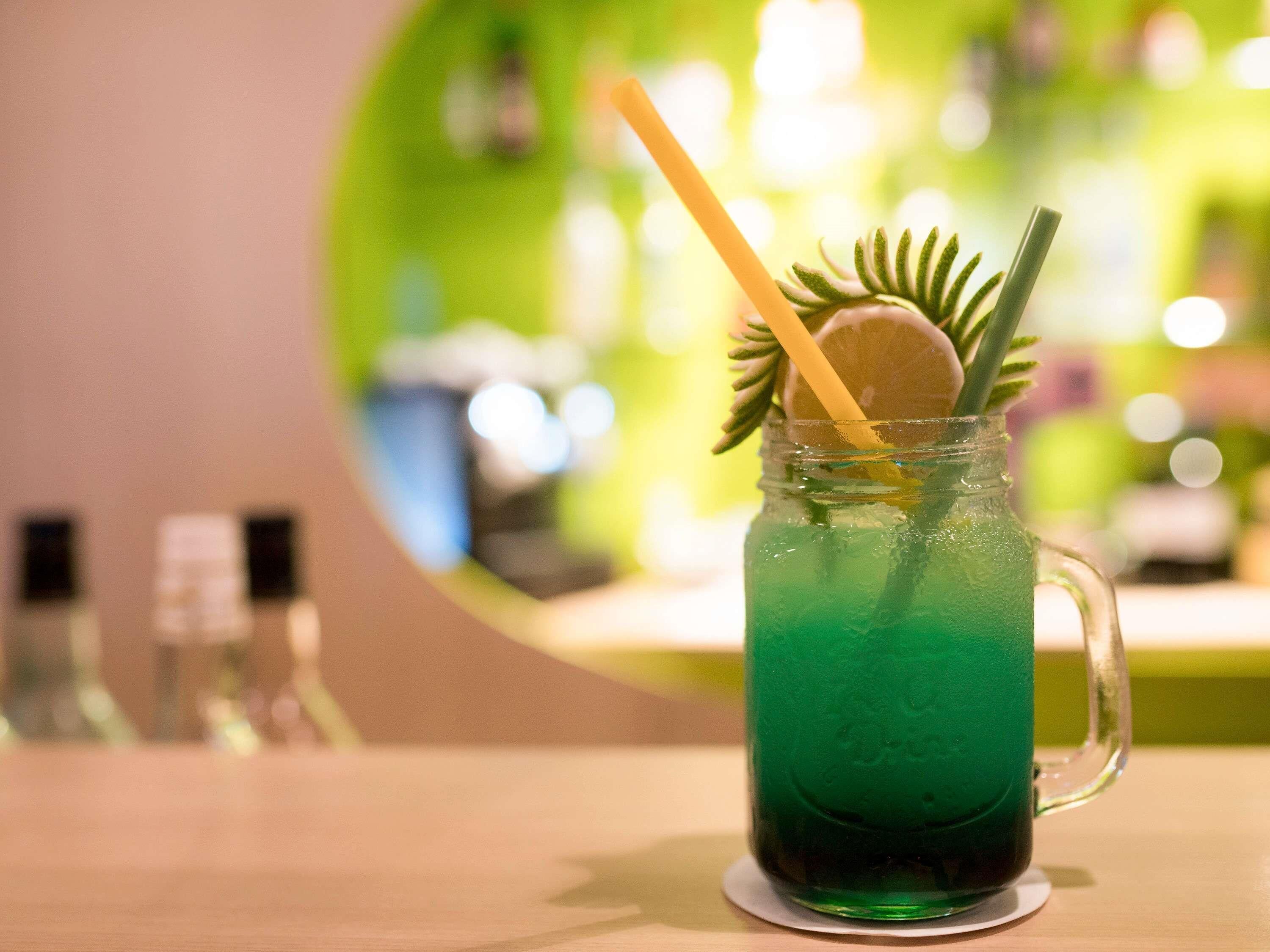 A green beverage in a glass mug with a straw and a slice of lime, placed on a wooden table.
