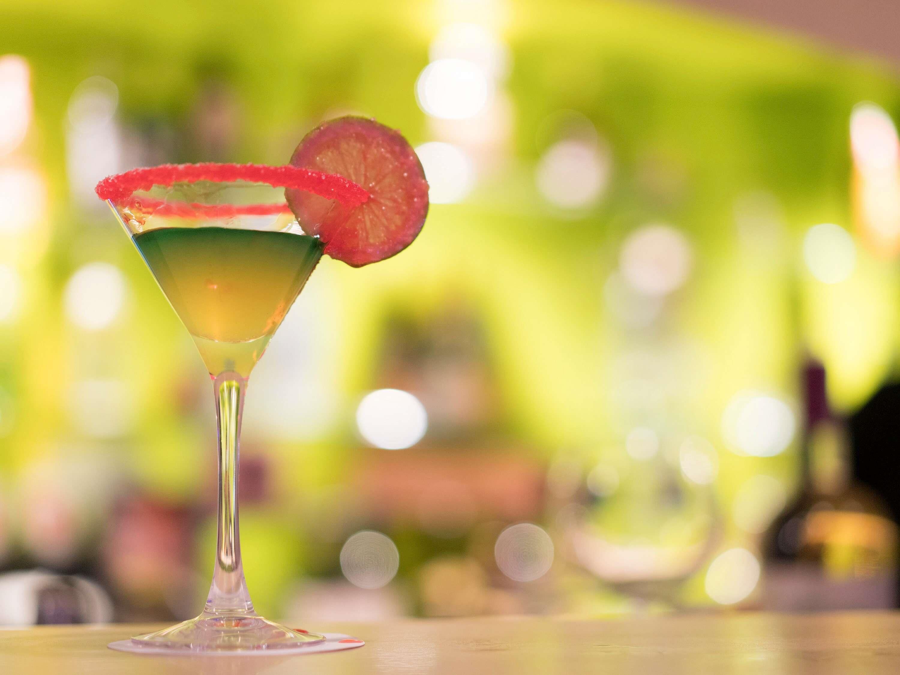 Un cocktail servi dans un verre à martini, avec un bord rouge et une tranche de fruit décorant le bord.