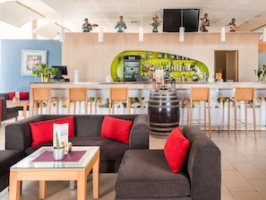 Una zona de bar con una barra verde, varios taburetes y un barril de madera grande.