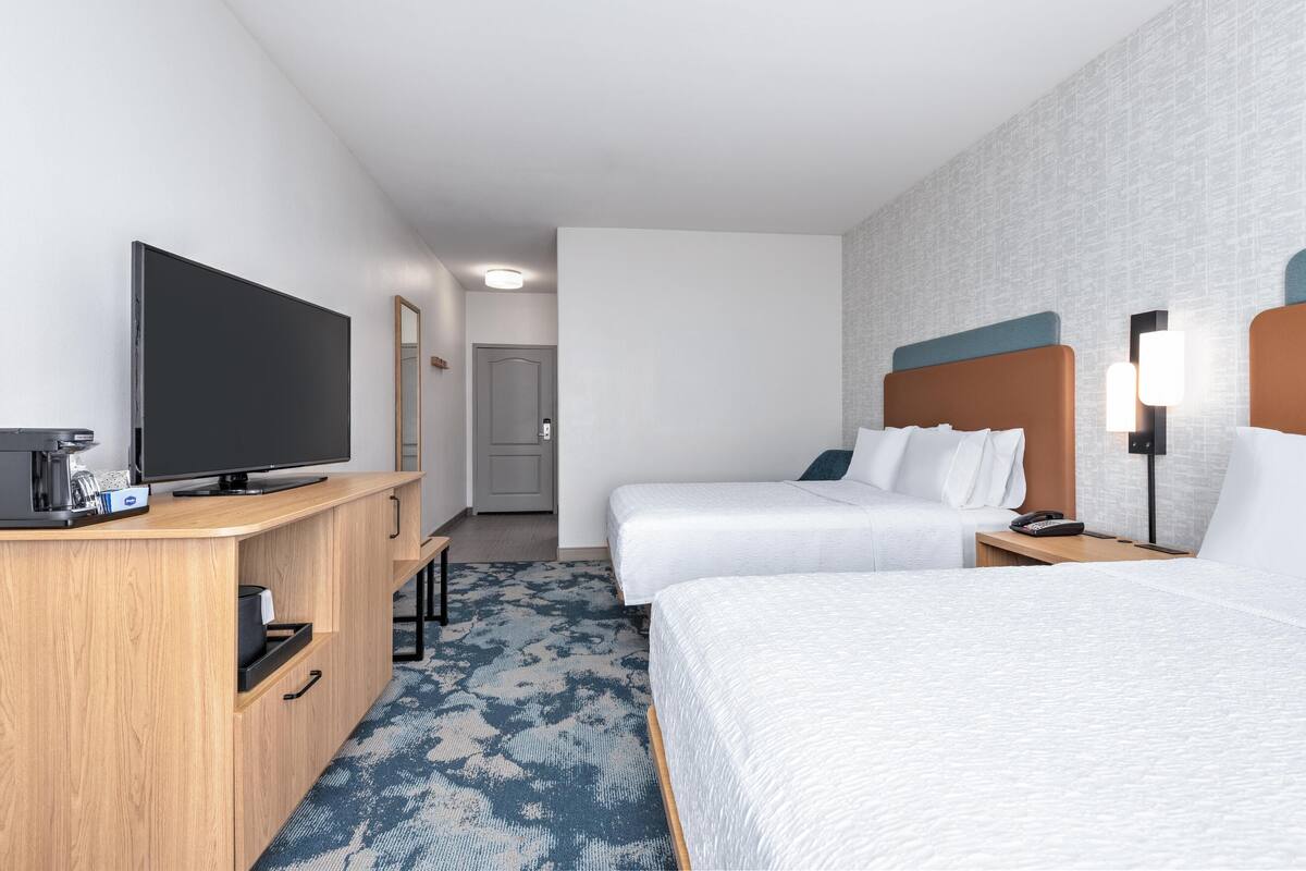 A hotel room with two beds, a TV, a desk with a coffee maker, and a patterned carpet.