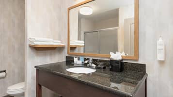 Un baño con lavamanos de encimera de granito, espejo y barra para toallas.