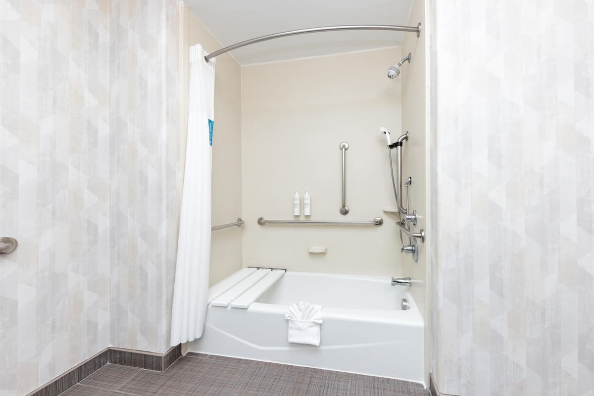 A modern bathroom with a walk-in shower, grab bars, a white bathtub, and a towel rack.