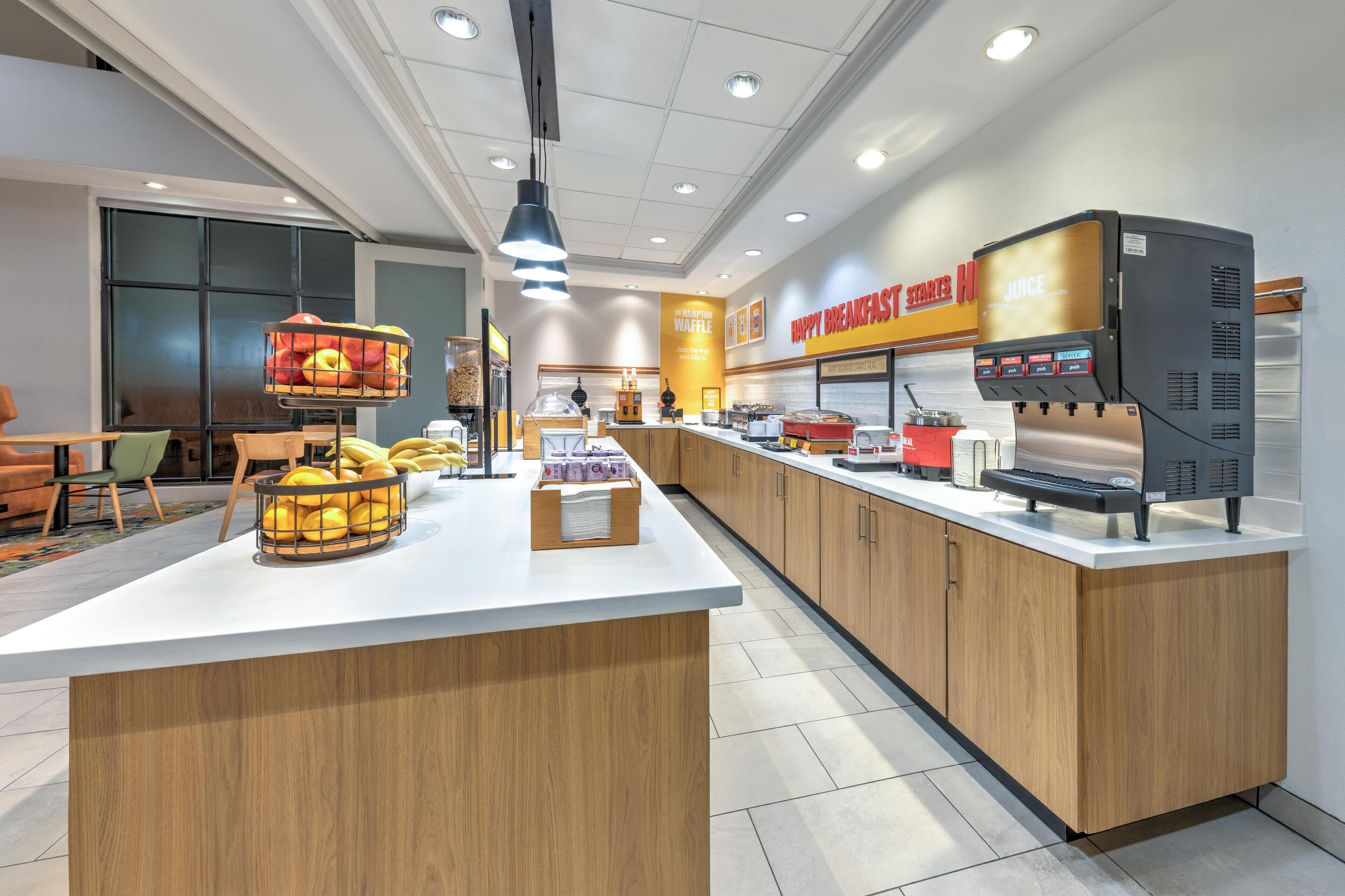 A modern breakfast area with a central island, a juice station, and a waffle station.