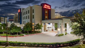 Et Hampton Inn & Suites hotel med en godt oplyst indgang, et overdækket udendørsområde og anlagte omgivelser.