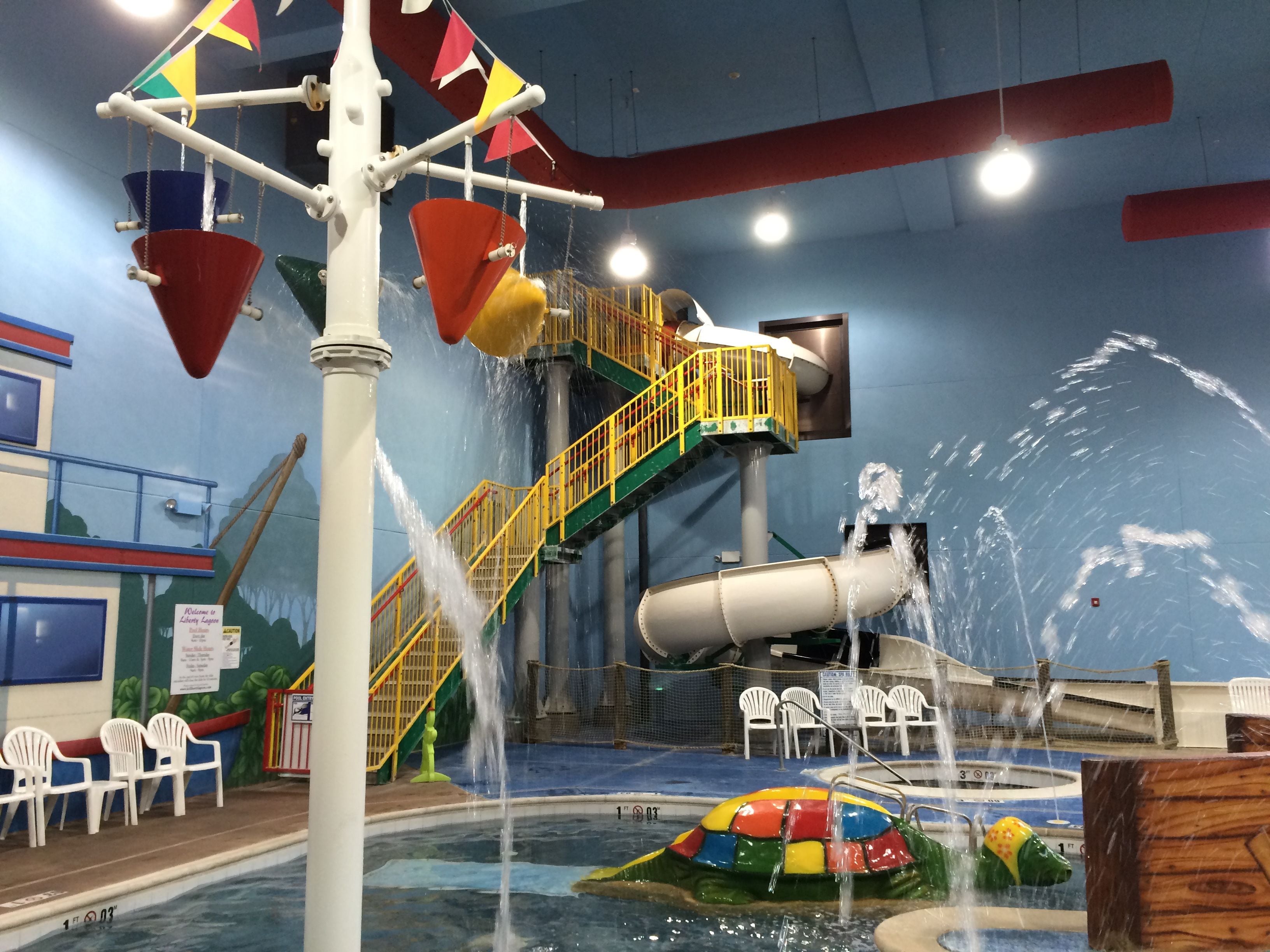Un parc aquatique intérieur comprenant un toboggan aquatique, une piscine et une structure de jeux colorée.