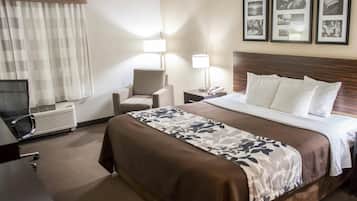 A hotel room with a bed, a chair, a desk, a lamp, and a wall with framed pictures.