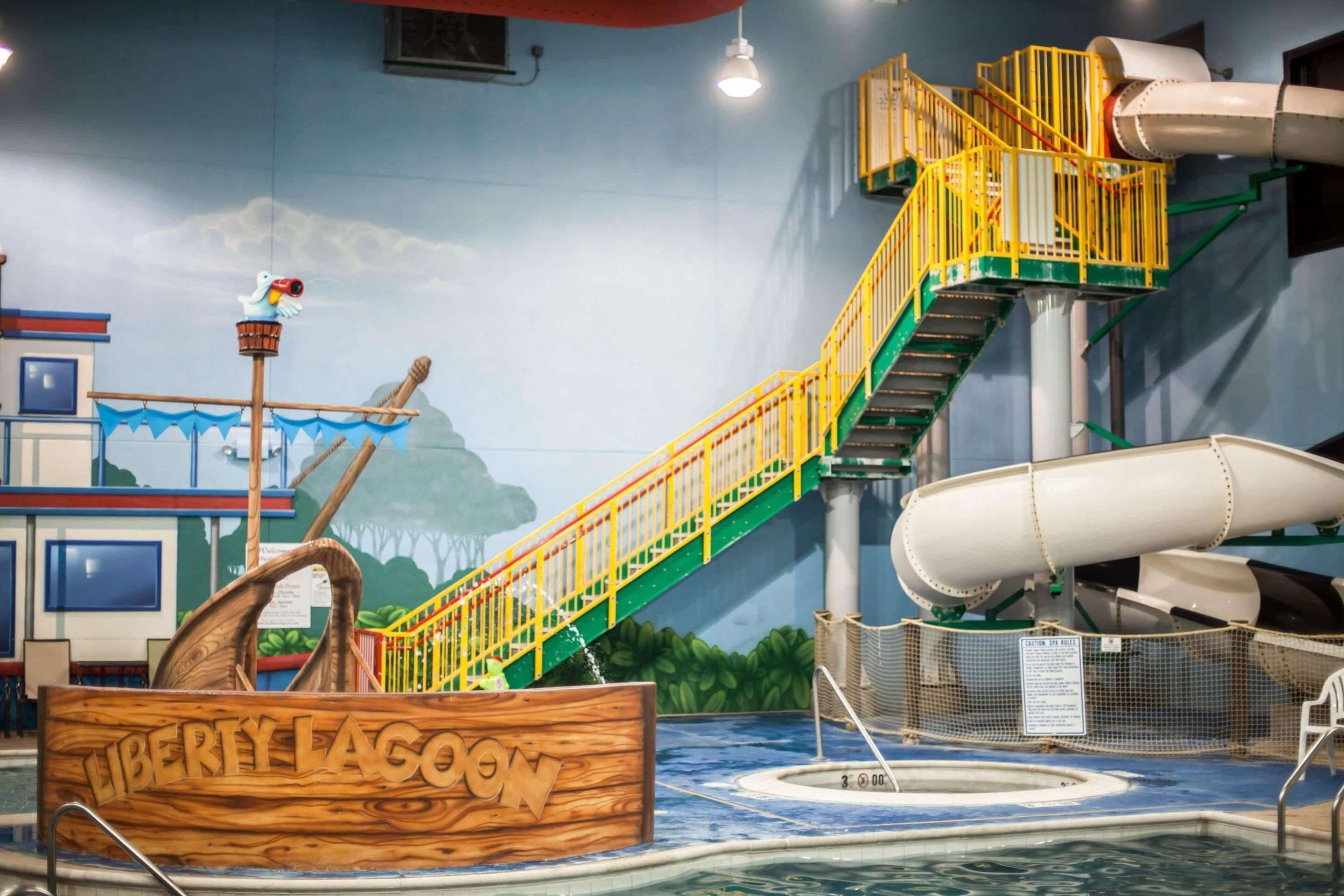 An indoor water park with a wooden boat labeled "LIBERTY LAGOON," a water slide, and a pool area.