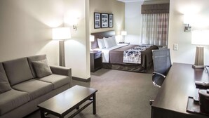Quarto de hotel com sofá, mesa pequena, cama com cabeceira, duas mesas de cabeceira com luminárias e escrivaninha com cadeira.