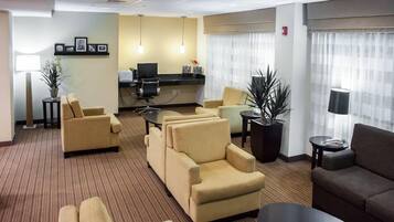 A hotel room with a seating area, a desk, and a computer.