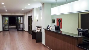 Uma área de recepção de hotel com um balcão de madeira, um computador Dell, um telefone e um sinal de saída de emergência vermelho.