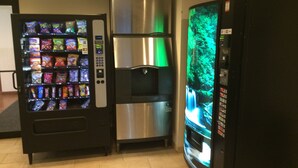 A vending machine with snacks, a stainless steel refrigerator, and a refrigerator with a green screen display.