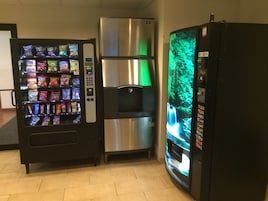 Máquina expendedora con aperitivos, un refrigerador de acero inoxidable y un refrigerador con pantalla verde.
