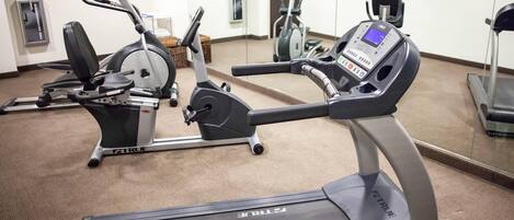 A gym with multiple exercise machines, including treadmills and stationary bikes, and a mirrored wall.