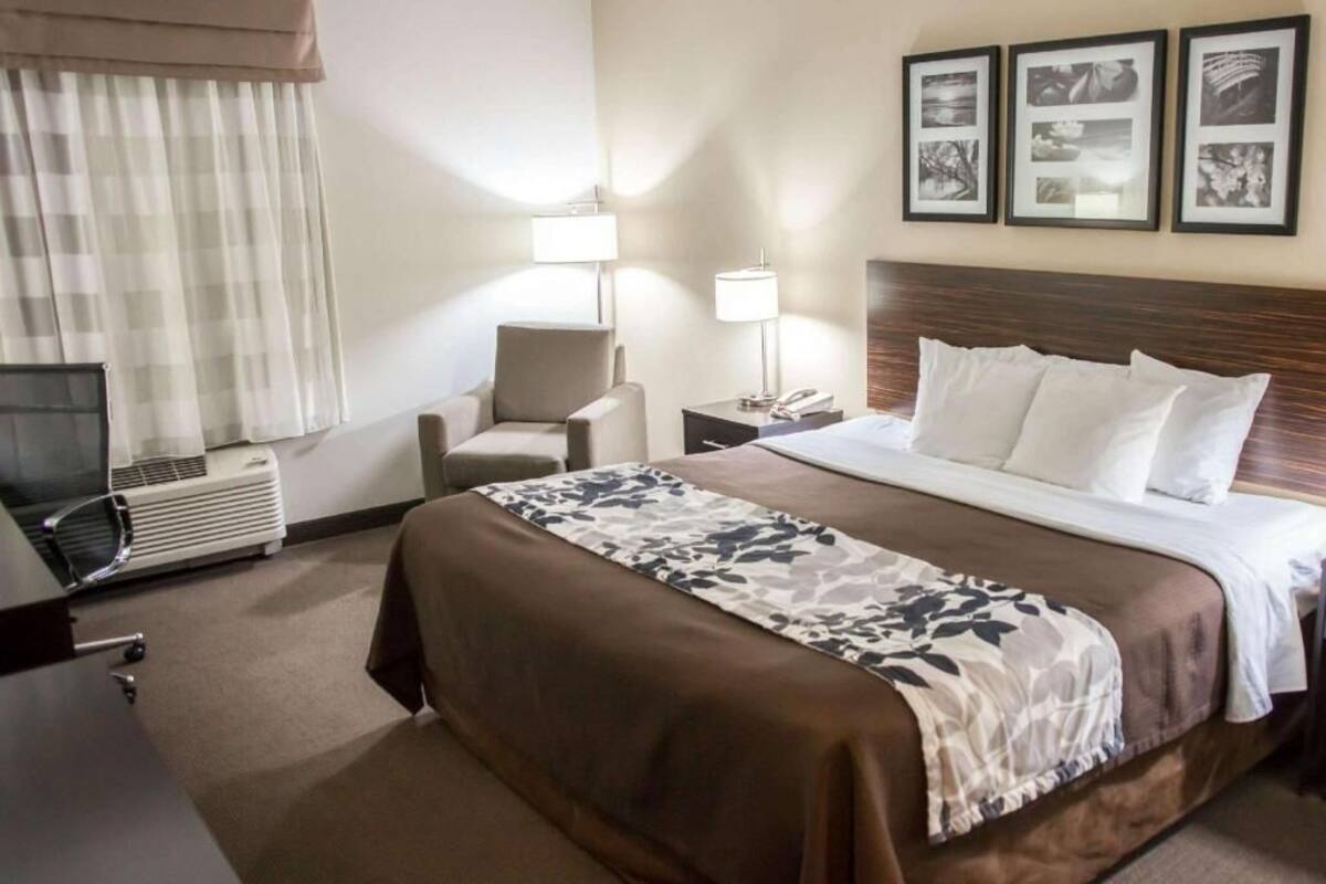 Une chambre d’hôtel avec un lit, une chaise, un bureau, une lampe et un mur orné de tableaux.