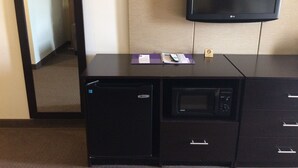 A hotel room with a desk, a microwave, a television, and a small refrigerator.