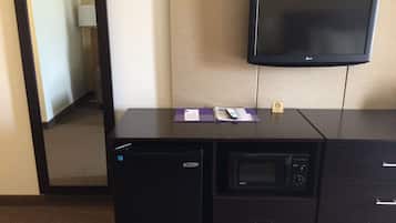 A hotel room with a desk, a microwave, a television, and a small refrigerator.