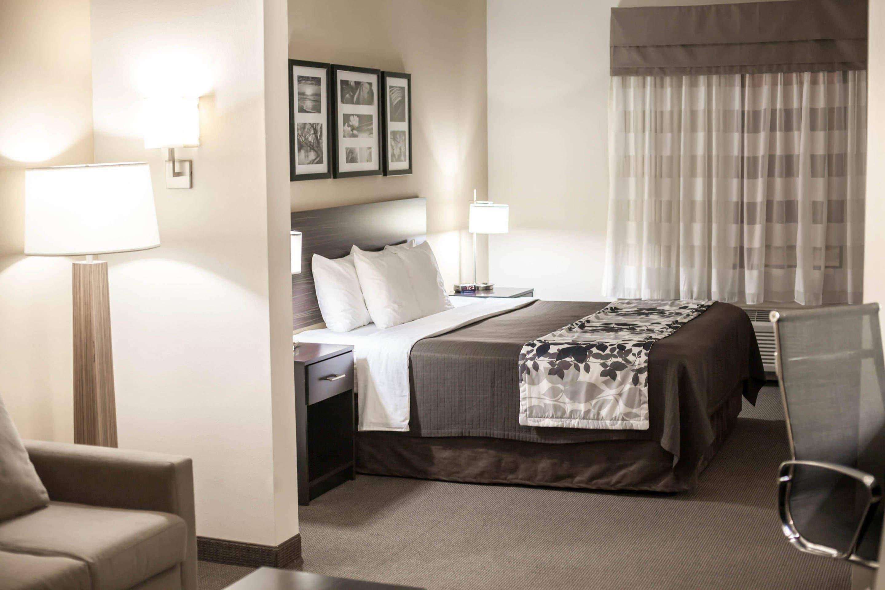 A hotel room with a bed, bedside tables, a lamp, a chair, and a window with curtains.