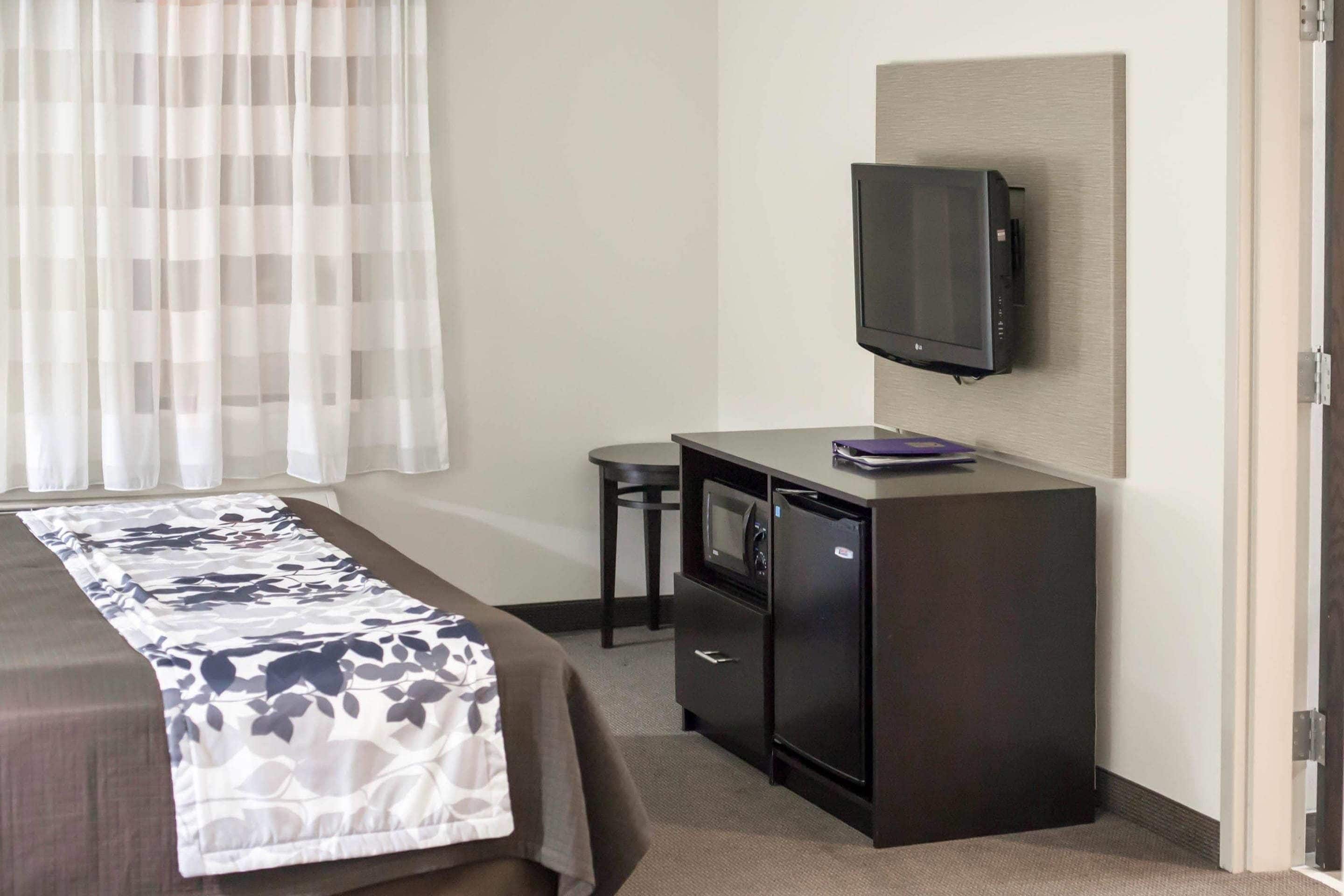 Una habitación de hotel con una cama, un escritorio con televisor, un microondas y un refrigerador.