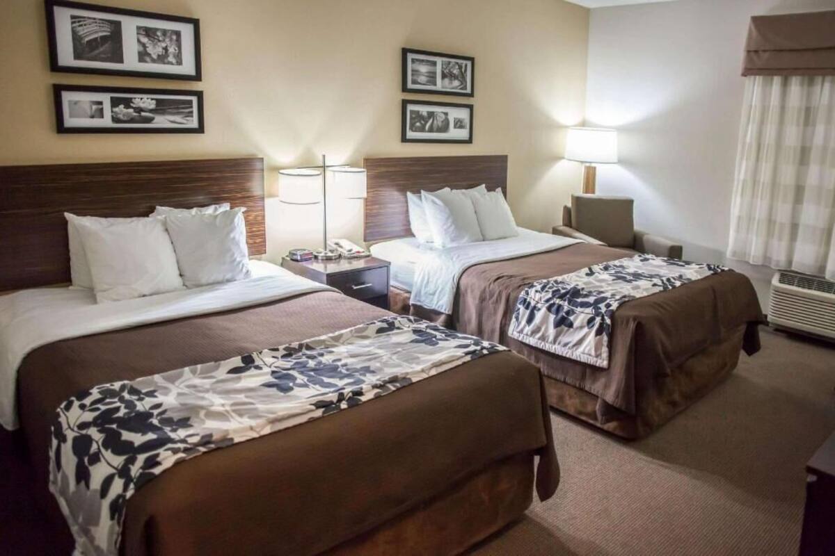 Une chambre d’hôtel avec deux lits, une table de chevet avec une lampe, un téléphone fixé au mur et des tableaux encadrés accrochés au mur.
