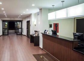 Zona de recepción de un hotel con un mostrador de madera, una computadora Dell, un teléfono y un tapete de bienvenida.