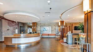 Een moderne hotellobby met een gebogen receptiebalie, een accentmuur van steen, een groot abstract schilderij en een zithoek met een kamerbreed tapijt.