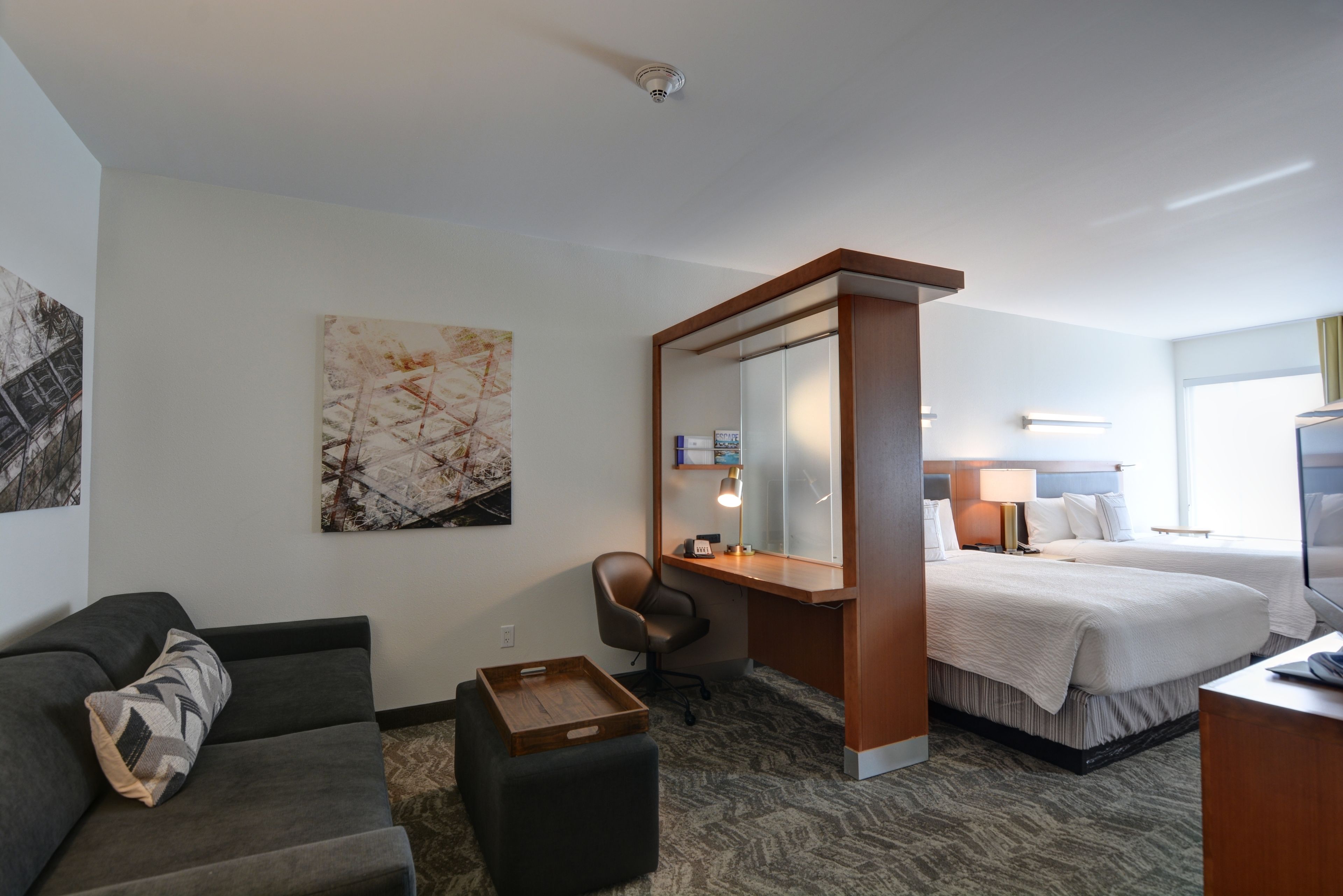 A hotel room with a bed, a desk with a chair, a sofa, a small wooden table, and a large mirror.