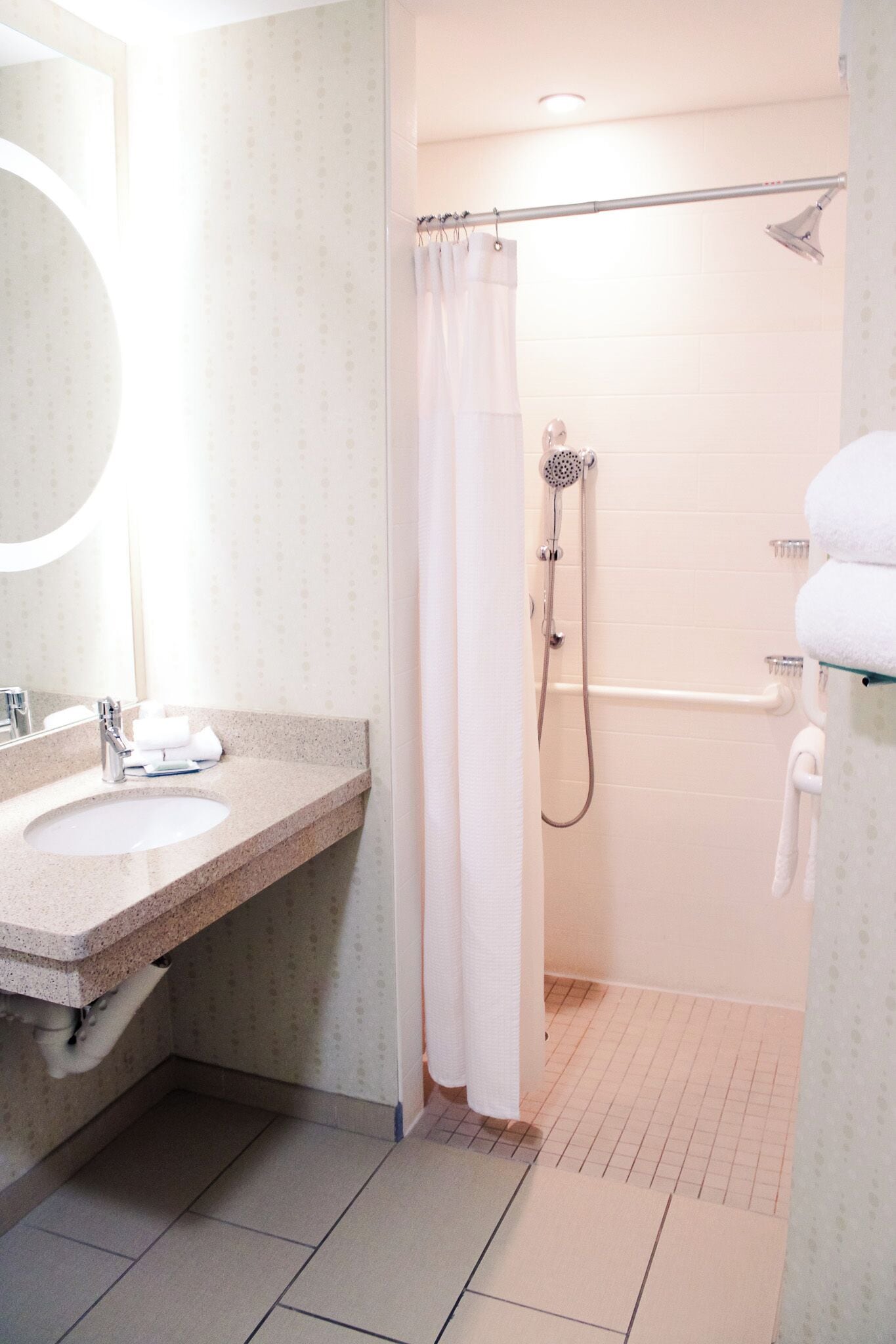 A bathroom with a sink, mirror, shower, and towel rack.