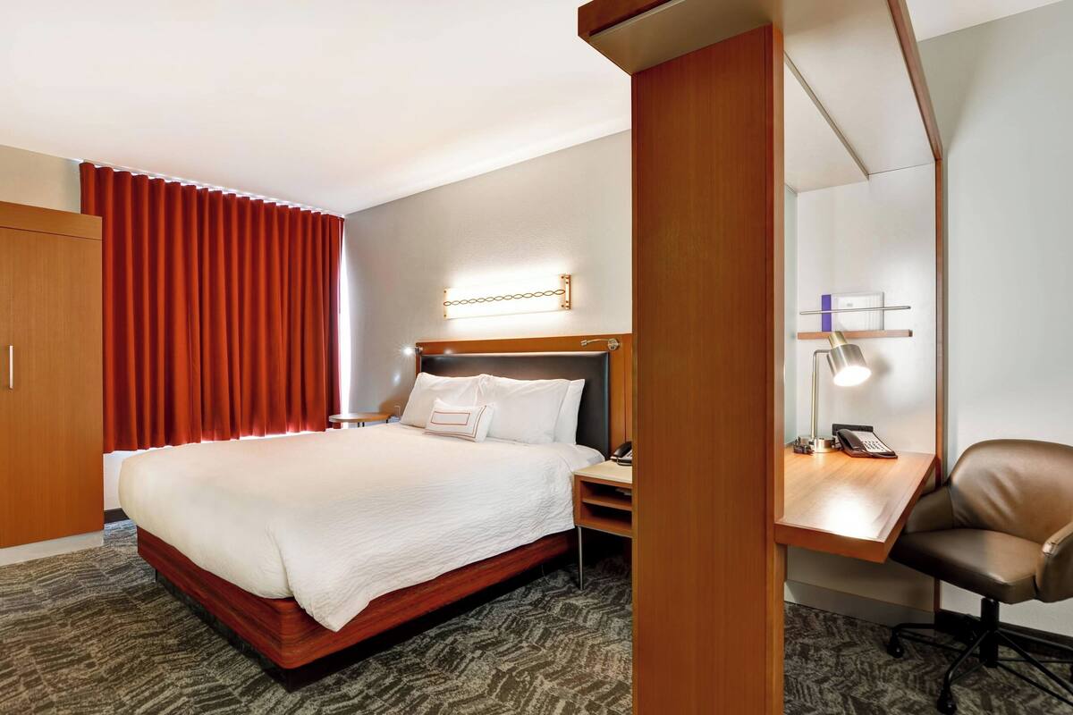 Ein Hotelzimmer mit einem Bett, einem Schreibtisch mit Stuhl, einer Schreibtischlampe und einem Telefon.