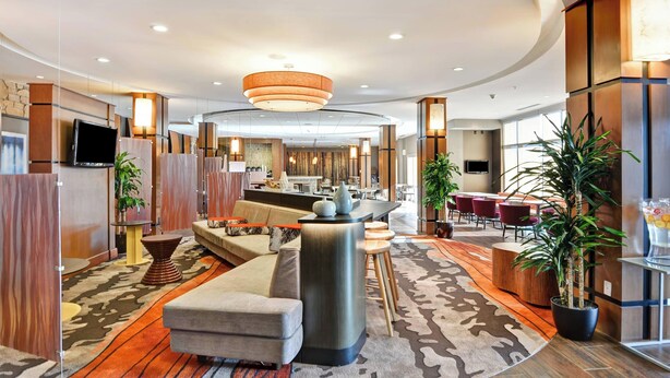 Een moderne hotellobby met een centrale zithoek, een bar en een eetgedeelte op de achtergrond.
