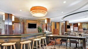 Een moderne bar met een stenen muur, een houten bar en drie houten krukken.