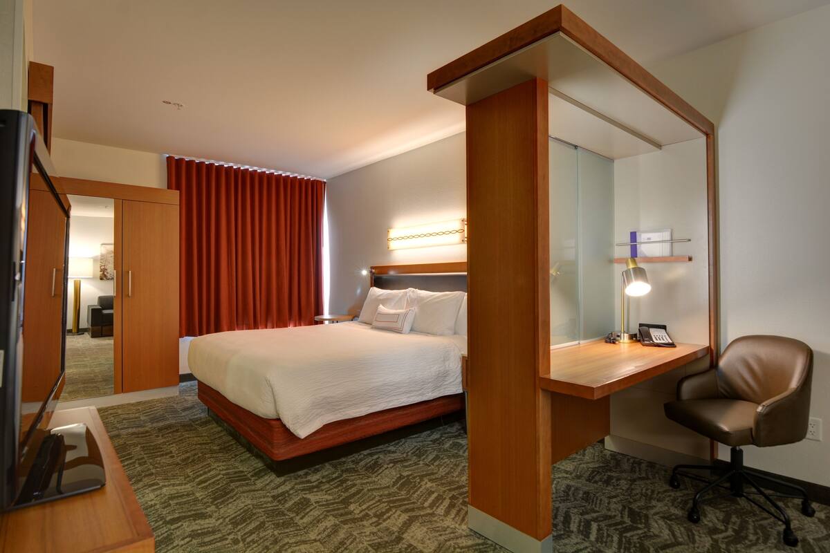 Ein Hotelzimmer mit einem Bett, einem Schreibtisch mit Stuhl, einem Spiegel und einem Fernseher.