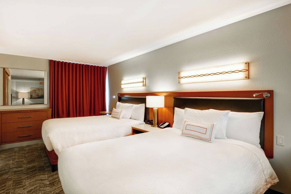 Ein Hotelzimmer mit zwei Betten, einem Schreibtisch, einem Spiegel und einem roten Vorhang.