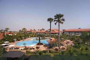 Een resort met een groot zwembad, palmbomen en meerdere gebouwen met rode daken.