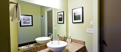 A bathroom with a double sink, a large mirror, framed pictures on the wall, and a towel hanging on the door handle.