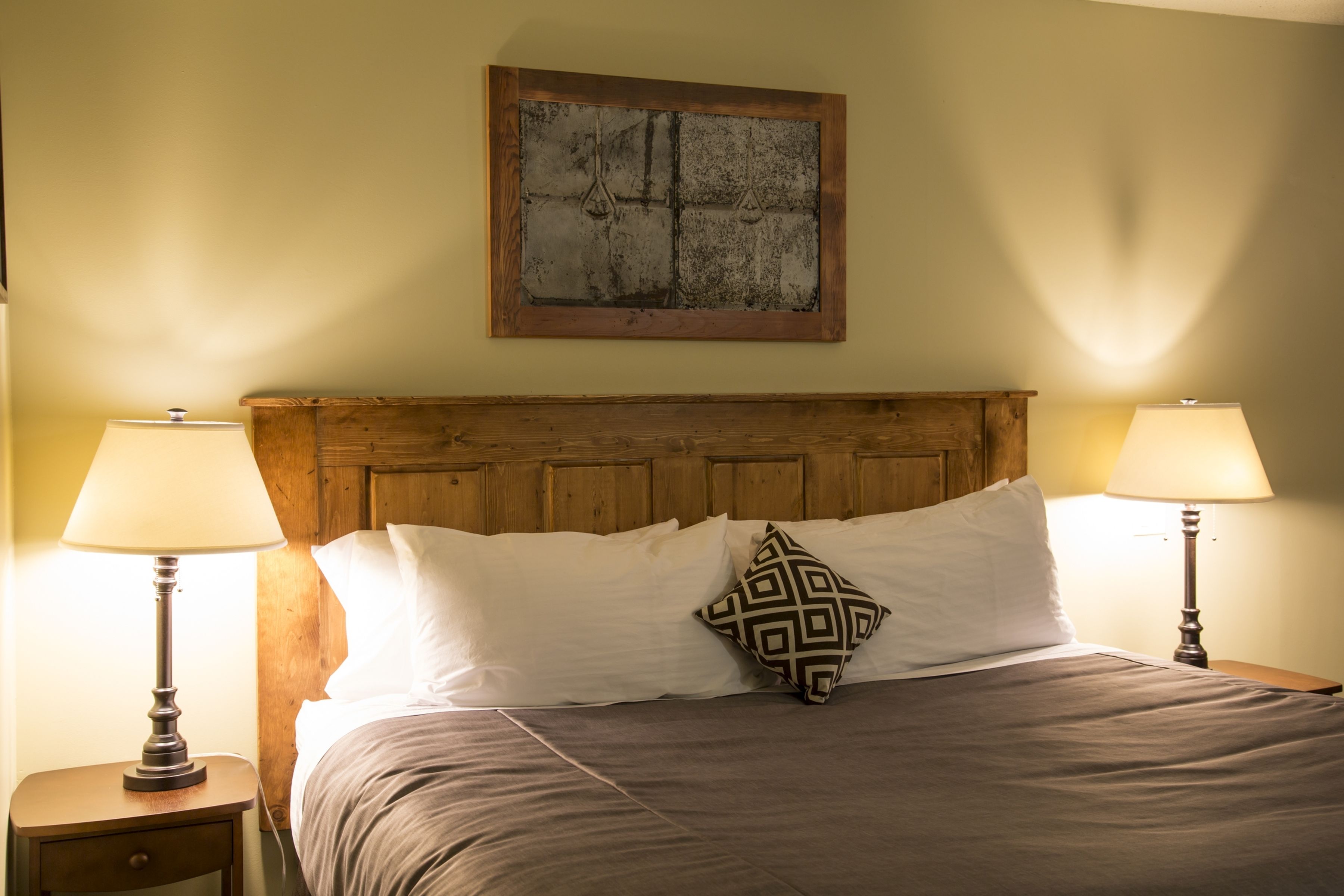 A neatly made bed with a wooden headboard, two bedside lamps, and a geometric patterned pillow.